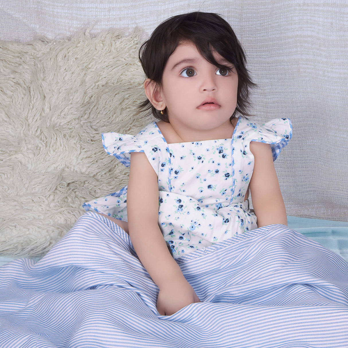 Baby girl in blue ruffle bloomer romper with back crossover straps and ruffles on the bottom