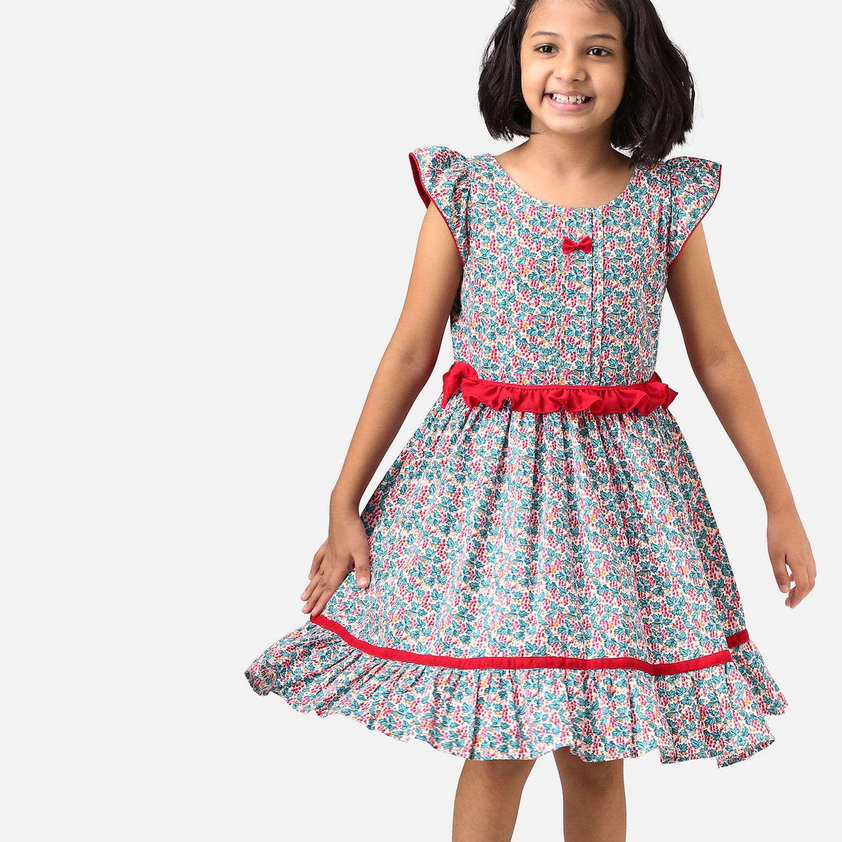 A girl in red and green floral printed cotton dress with a tie up fabric ruffle belt