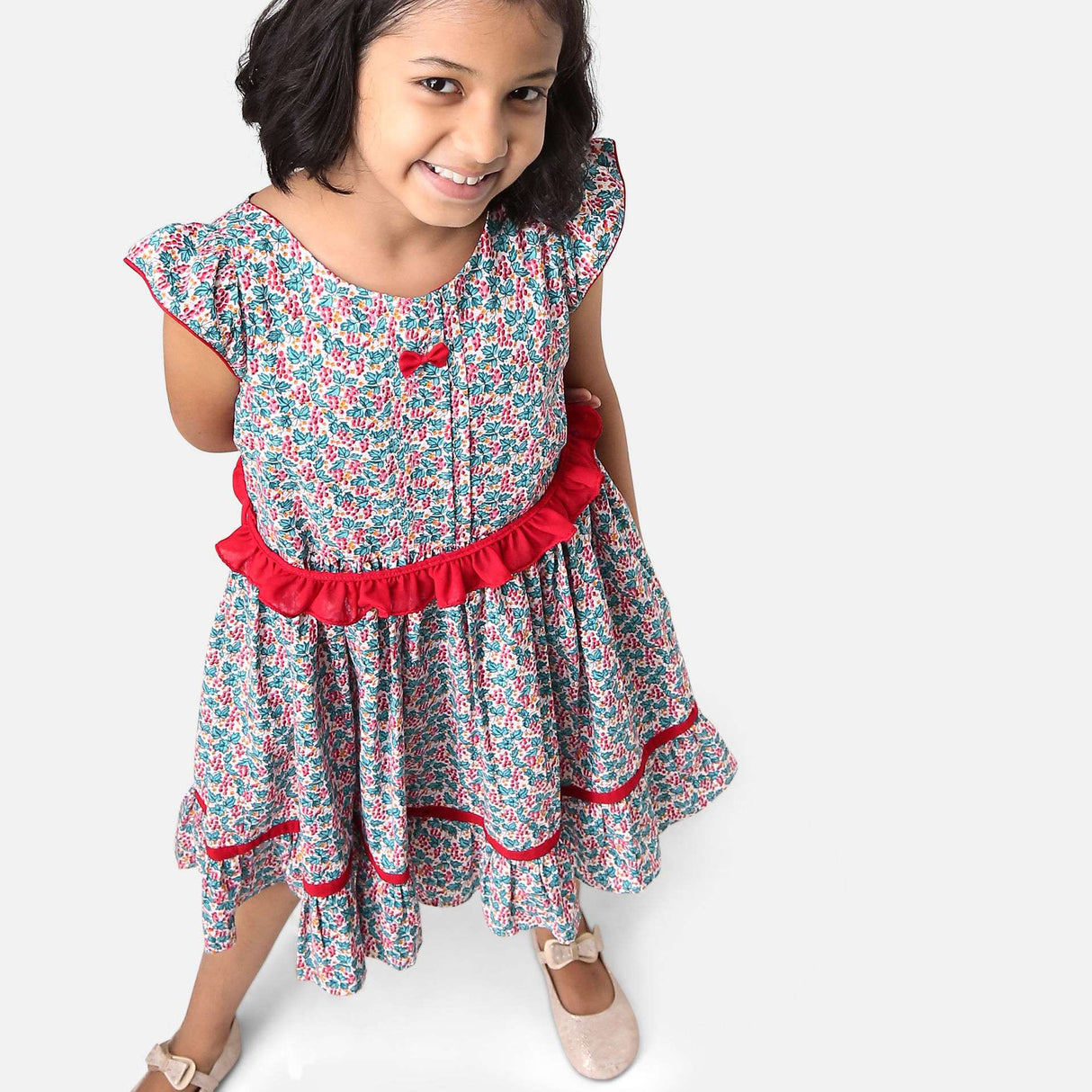 A girl in red and green floral printed cotton dress with a tie up fabric ruffle belt