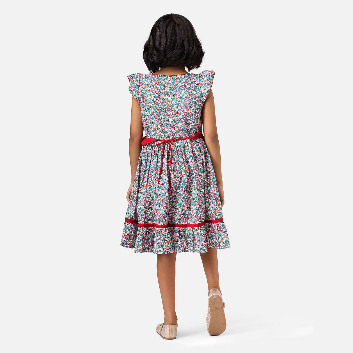 A girl in red and green floral printed cotton dress with a tie up fabric ruffle belt