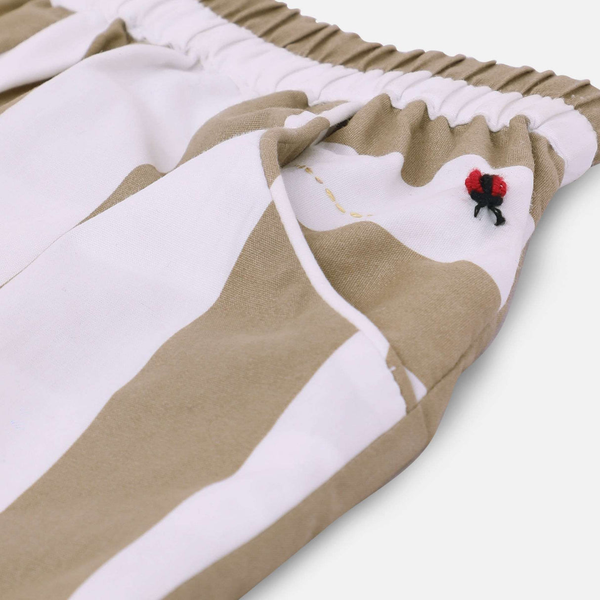 Close-up of lady bird embroidery on the pocket of scallop hem shorts in tan and white stripes