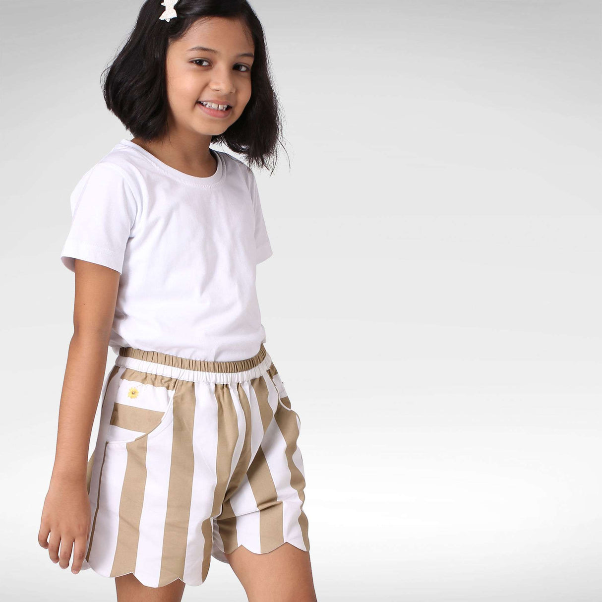 Girl wearing a tan and white broad stripe scallop shoorts with side pockets and embroidery