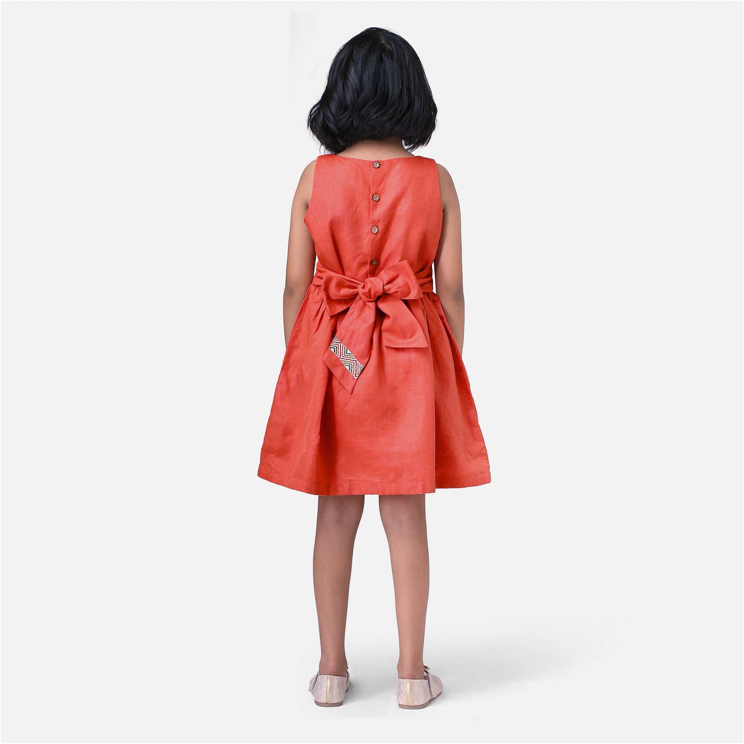 A girl in chic burnt-orange linen dress with colourful embroidered waistline with a Kantha-work hand-embroidered bodice