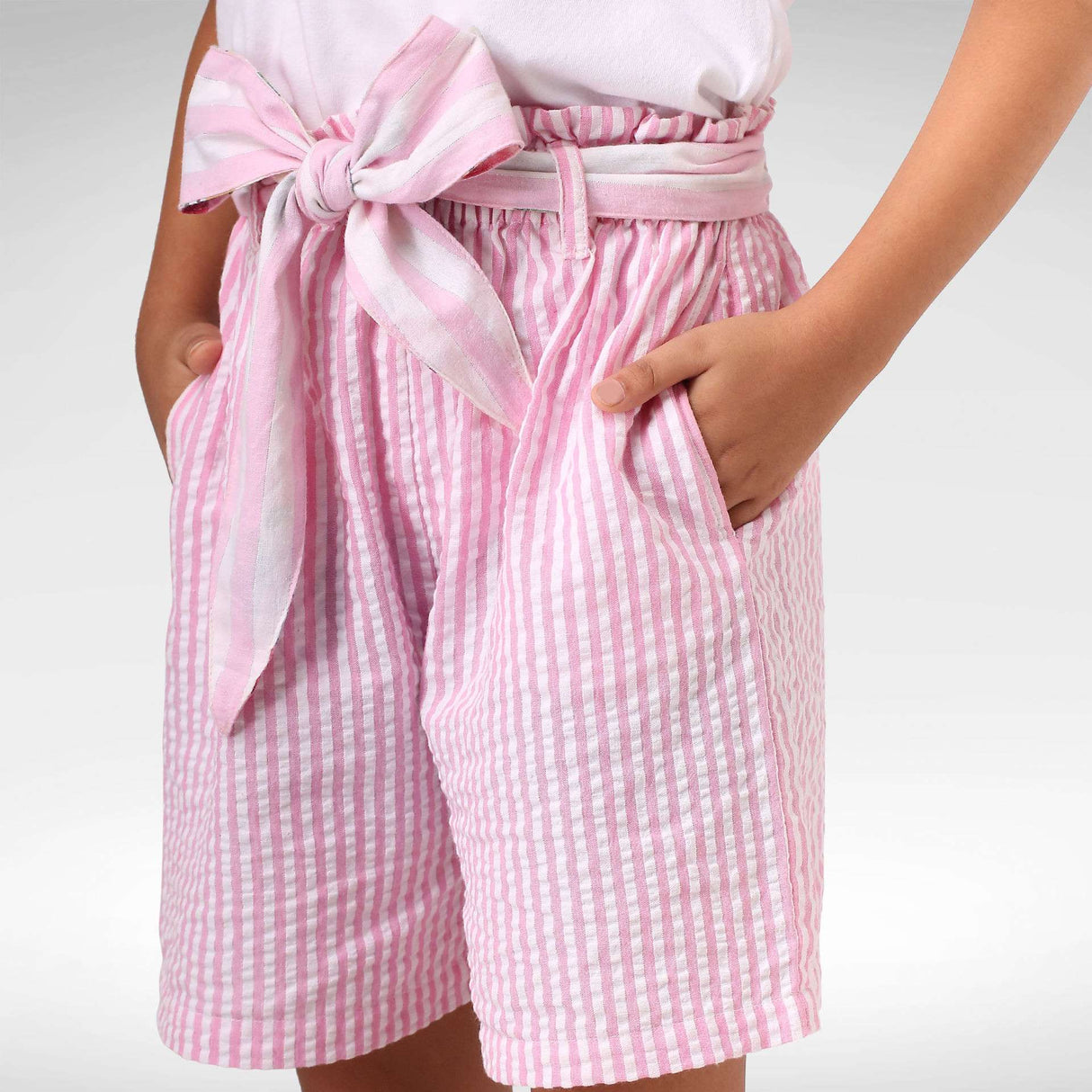 Girl wearing pink seersucker stripe shorts with hands in pocket and a pink stripe belt