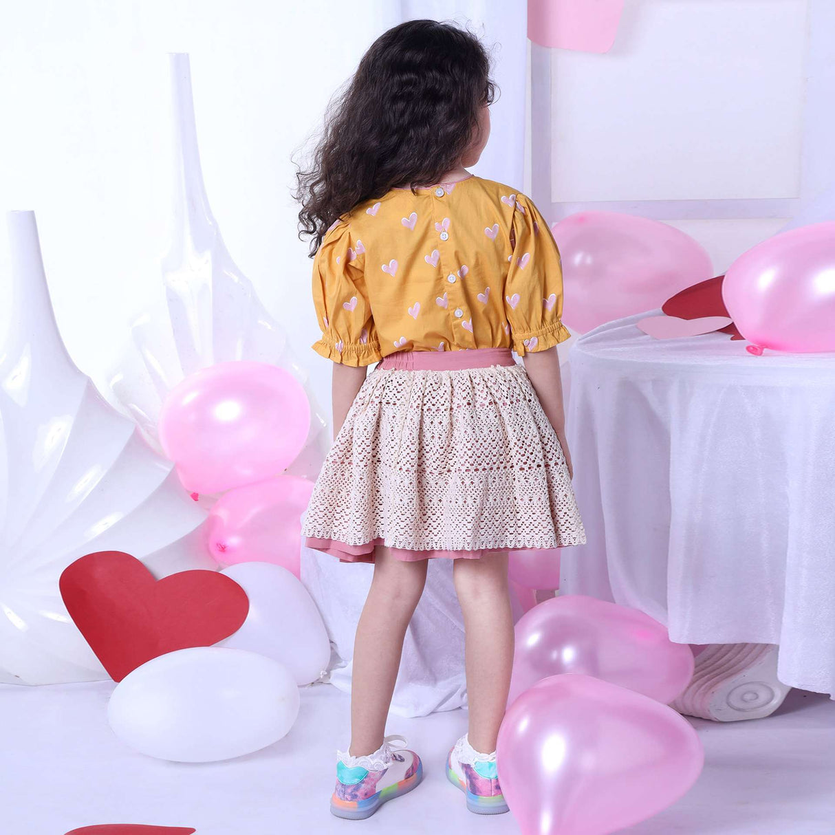 Backside image of girl in blouse with a heart print on a wheat gold base and ivory lace skirt with pink underskirt
