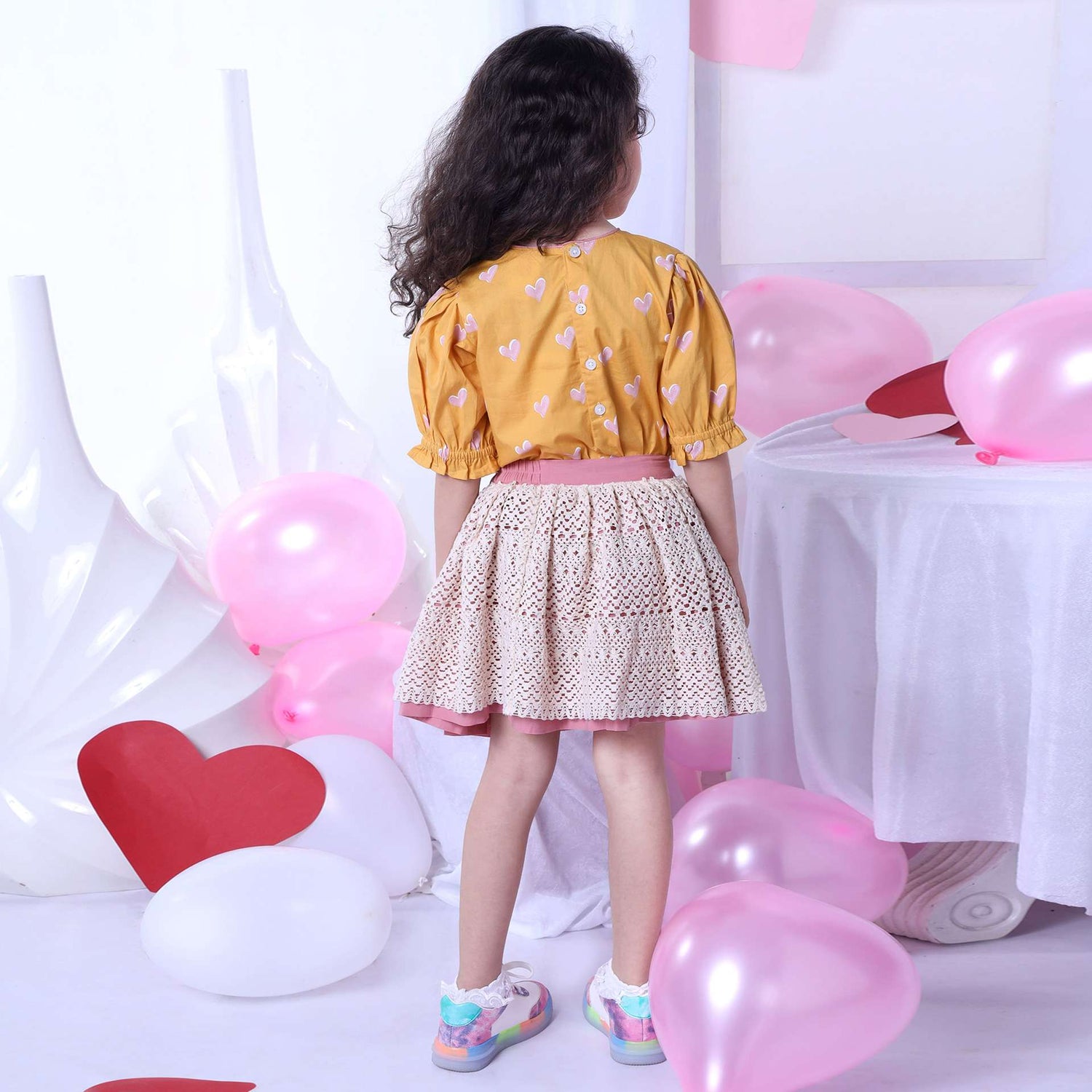 Backside image of girl in blouse with a heart print on a wheat gold base and ivory lace skirt with pink underskirt