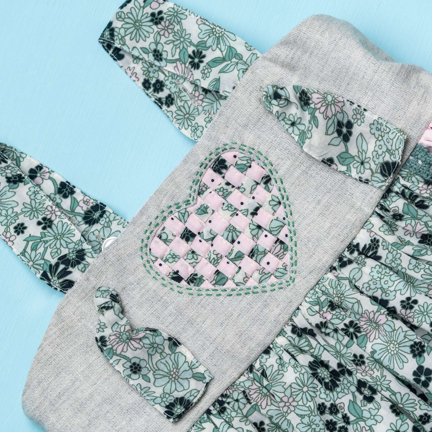 Close-up image of strappy dress with floral print and pink dot fabric with intricate ribbon patchwork heart applique