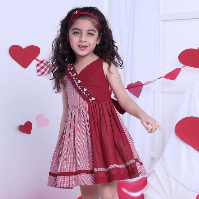 A girl in red checked dress with a hand-smocked band of hearts in a crossover style, with a V-neck and cord piping trims