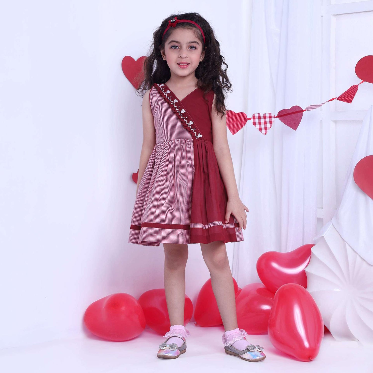 A girl in red checked dress with a hand-smocked band of hearts in a crossover style, with a V-neck and cord piping trims