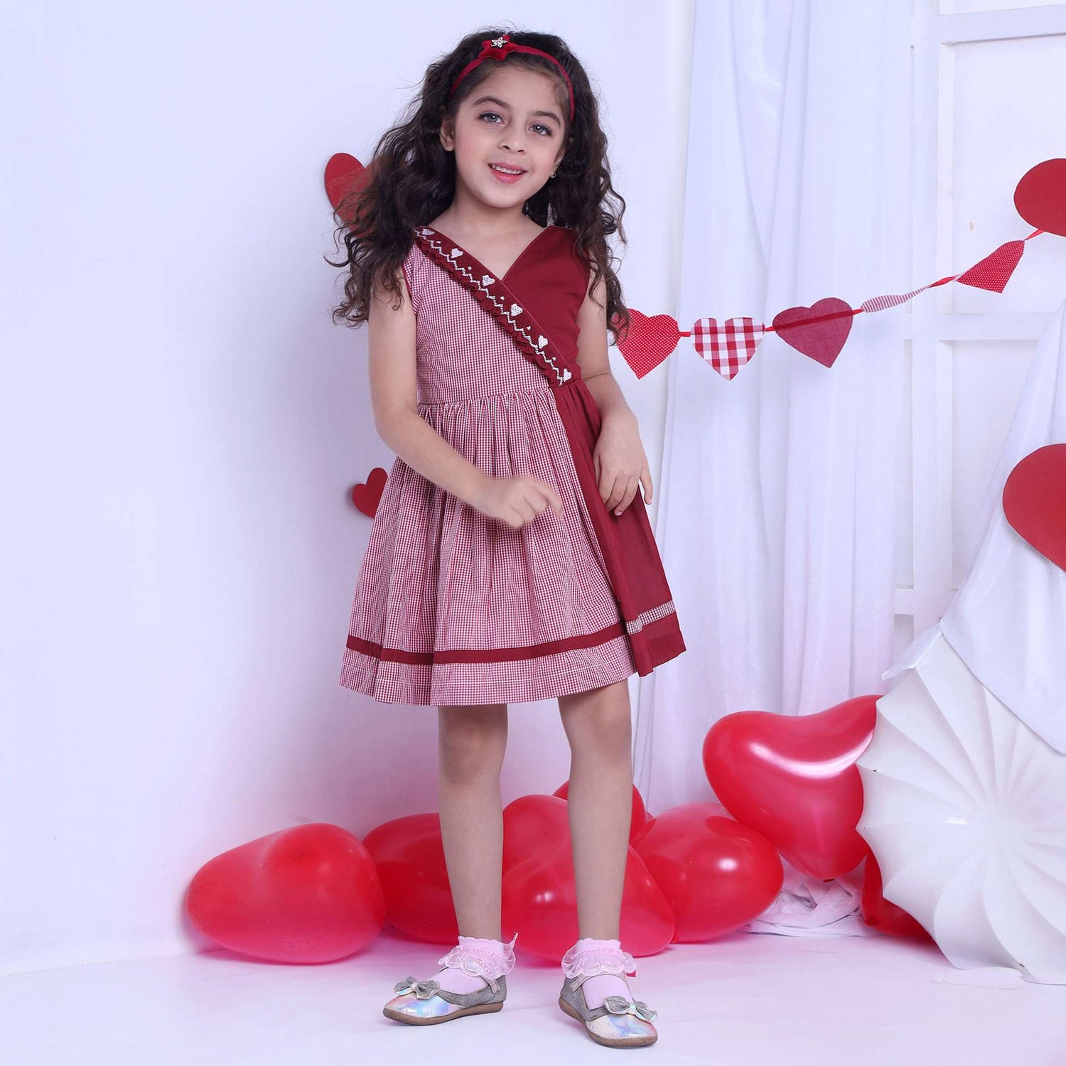 A girl in red checked dress with a hand-smocked band of hearts in a crossover style, with a V-neck and cord piping trims