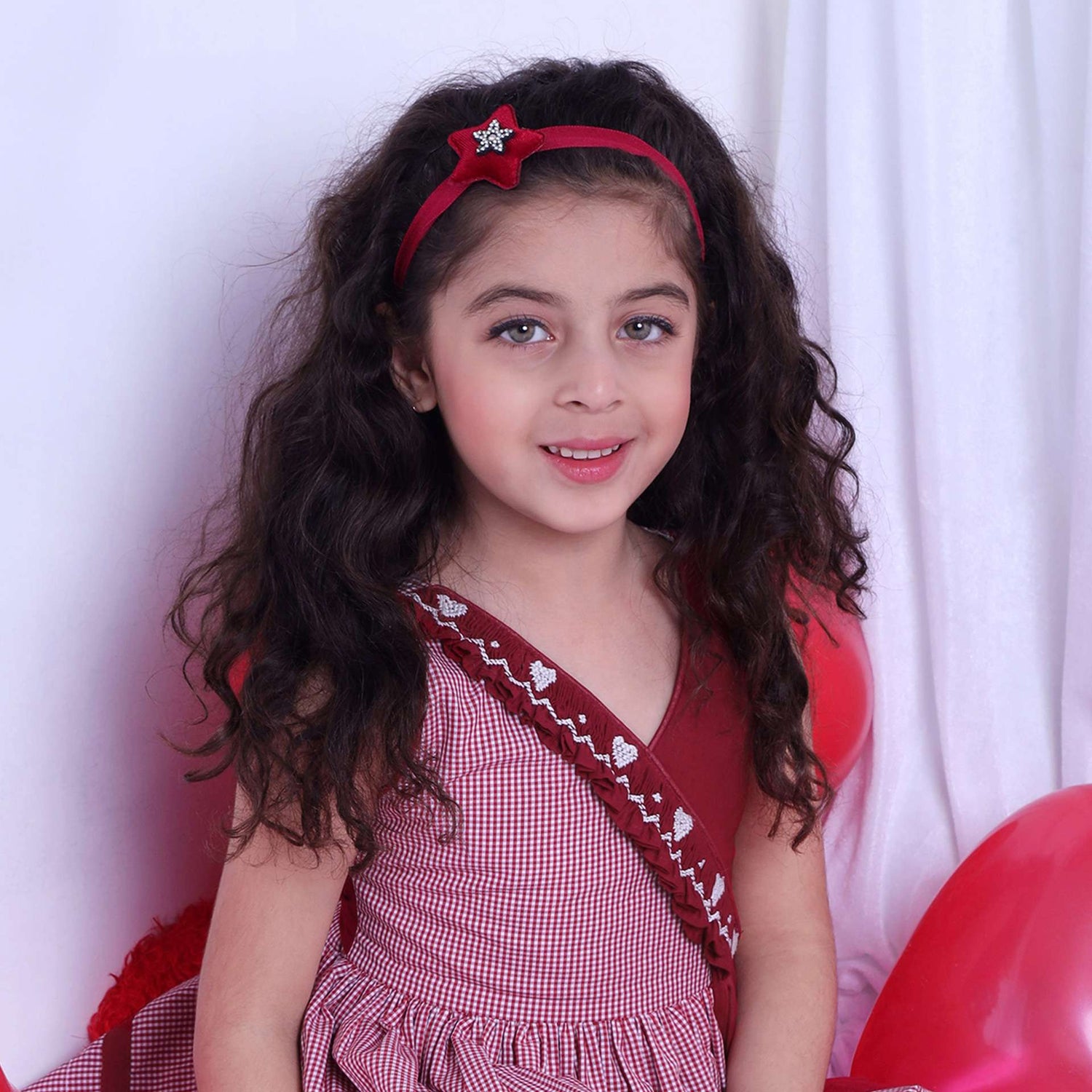 A girl in red checked dress with a hand-smocked band of hearts in a crossover style, with a V-neck and cord piping trims