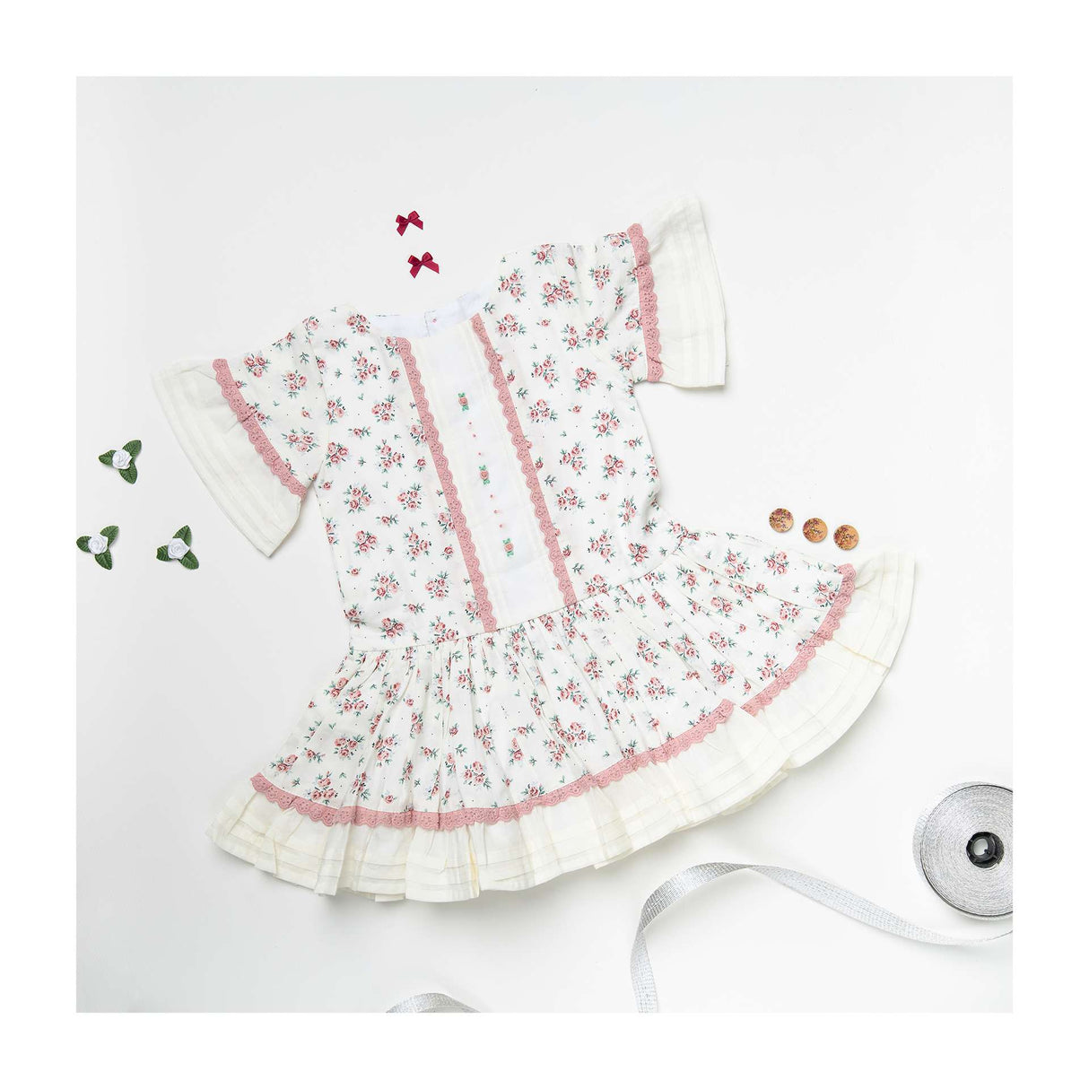 Flatlay of ivory floral-spray printed dress with hand embroidery, dropwaist pattern with pleated hem ruffles
