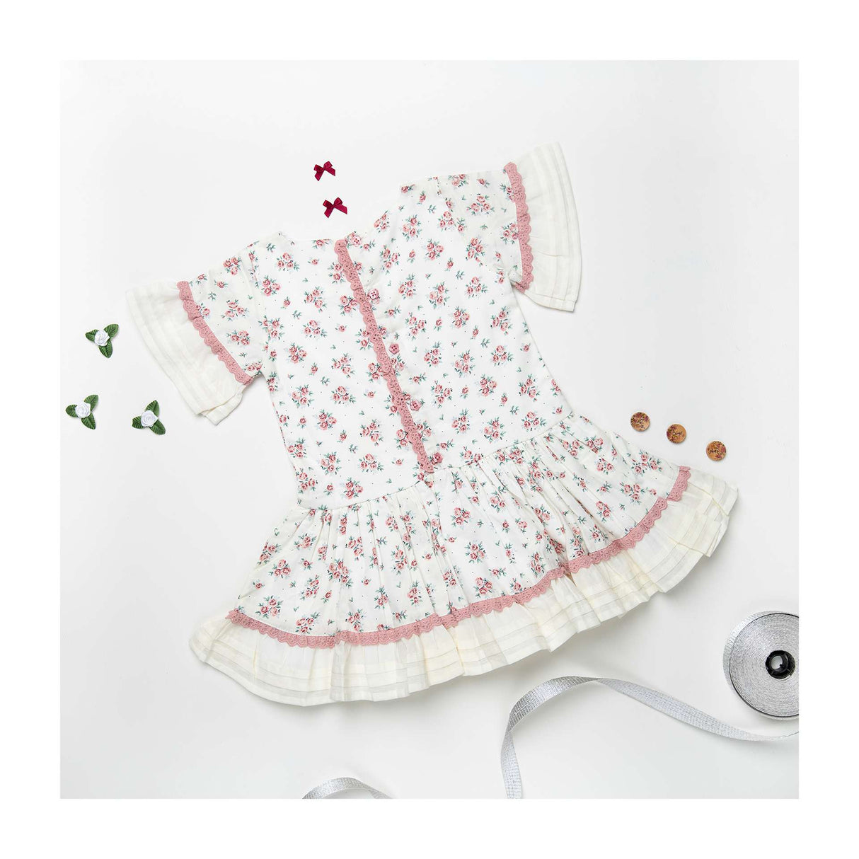 Flatlay of ivory floral-spray printed dress with hand embroidery, dropwaist pattern with pleated hem ruffles