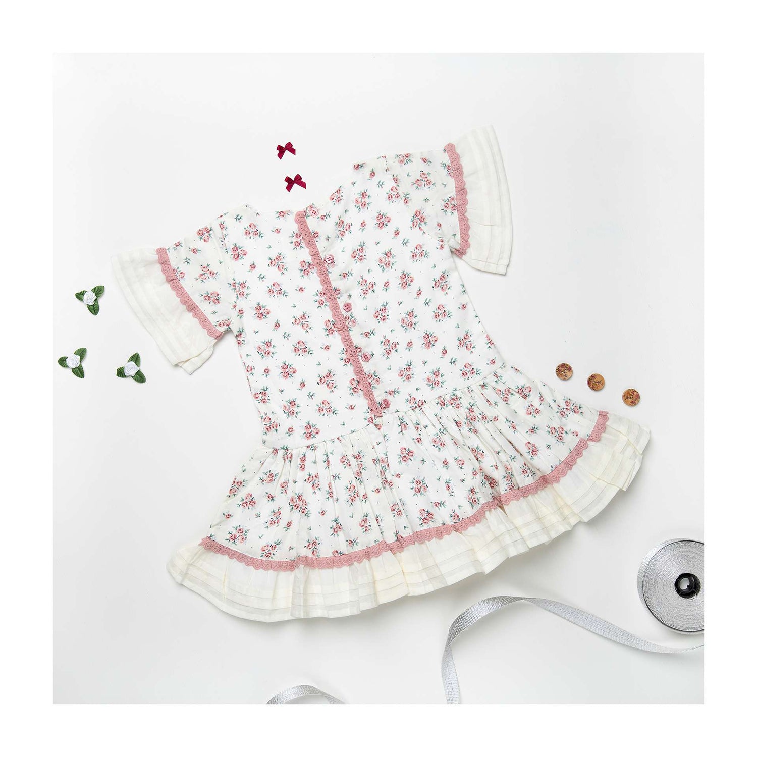 Flatlay of ivory floral-spray printed dress with hand embroidery, dropwaist pattern with pleated hem ruffles