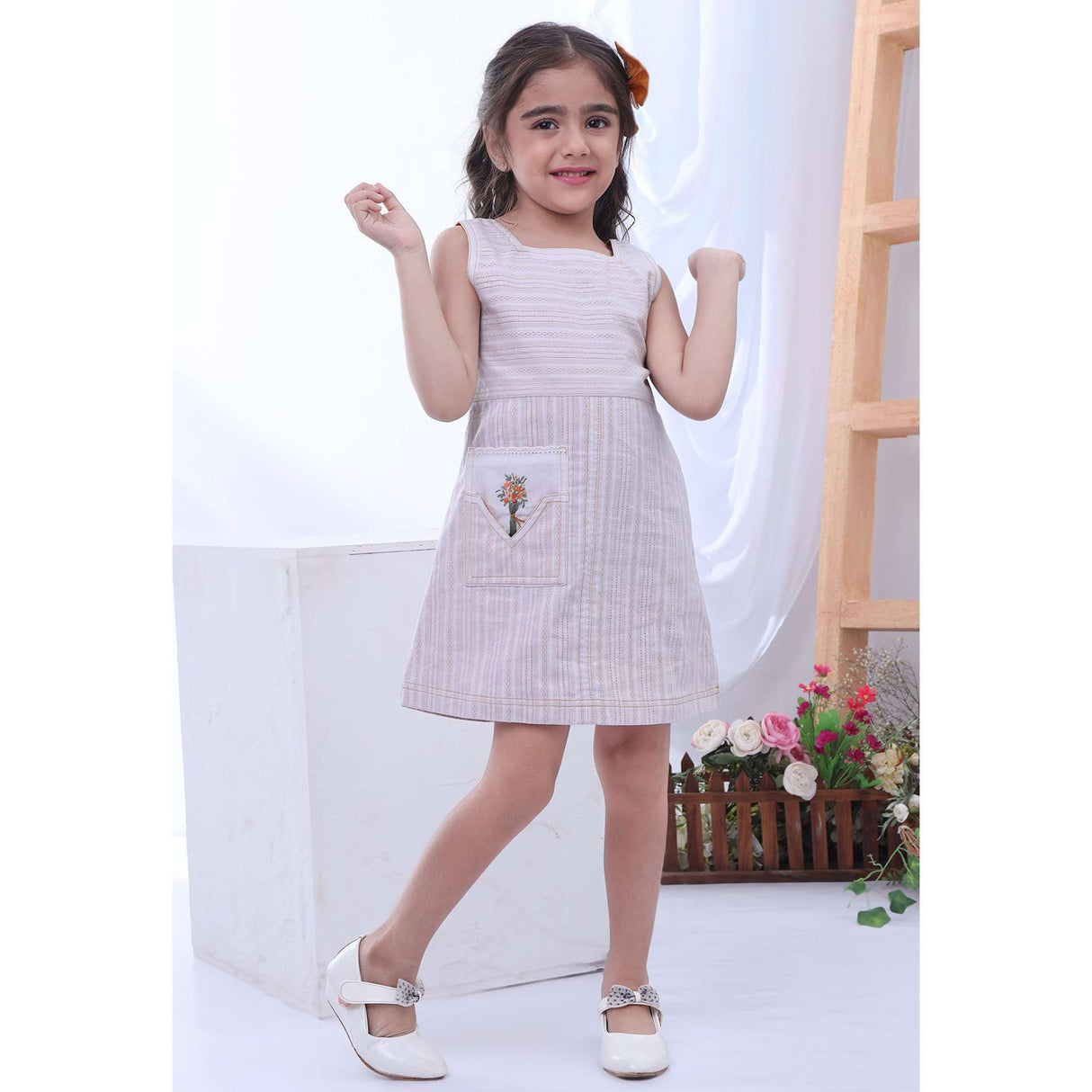 A little girl in sleeveless dress with hand embroidered bouquet on front pocket