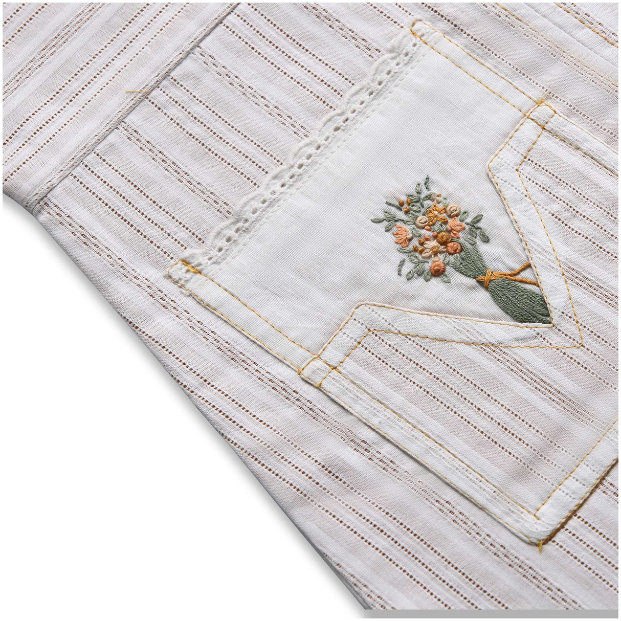 Close up of cream dress with mustard lining and side pocket with lace trims embellished with embroidered bouquet