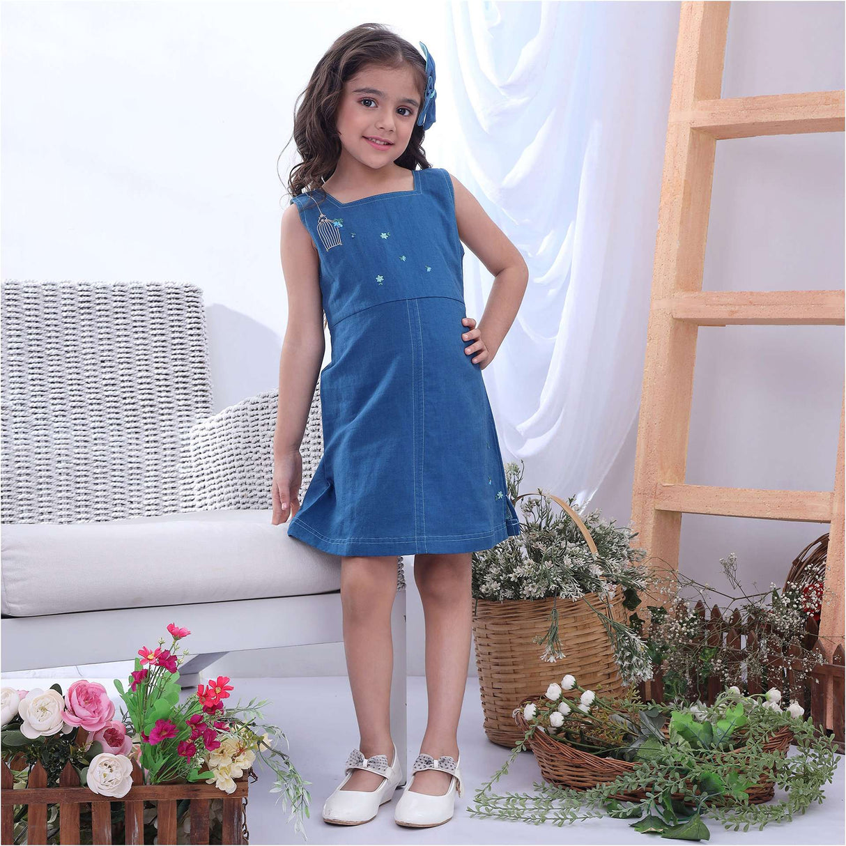 A girl in a blue sleeveless dress with a hand embroidered bird cage and some scattered flowers
