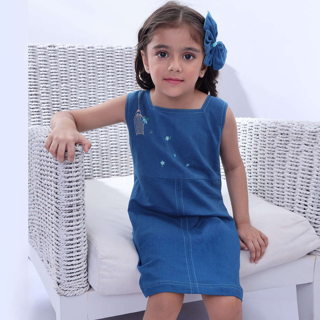 A girl in a blue sleeveless dress with a hand embroidered bird cage and some scattered flowers