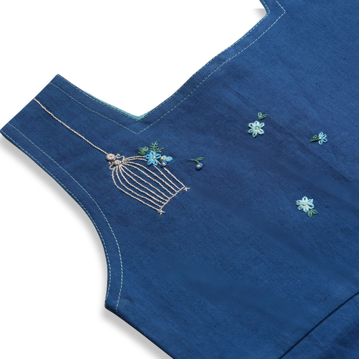 Close up of blue sleeveless dress with a hand embroidered bird cage and some scattered flowers