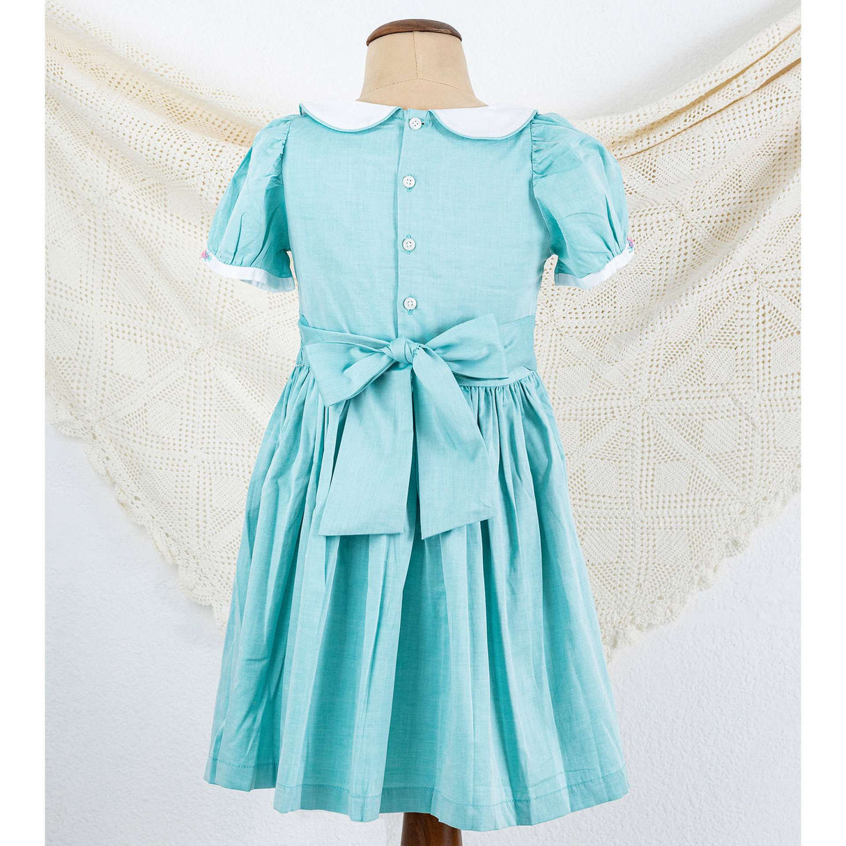 Mannequin 's rear side in turquoise classic smocked girls dress with back ties tied into a bow