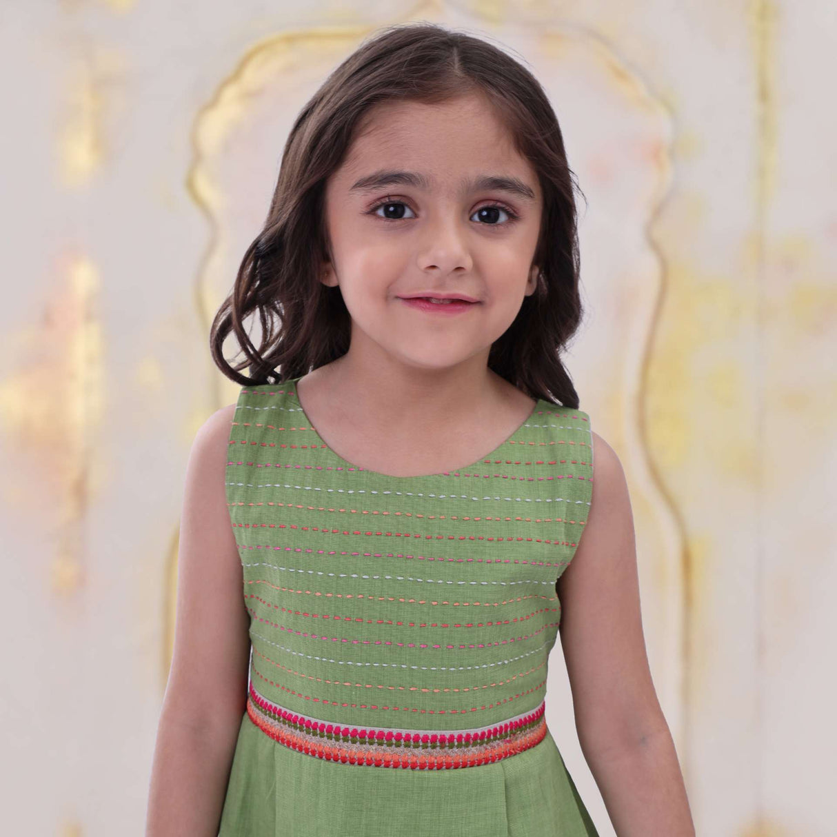Close up of a little girl in green sleeveless dress with hand embroidered border detail and back belt