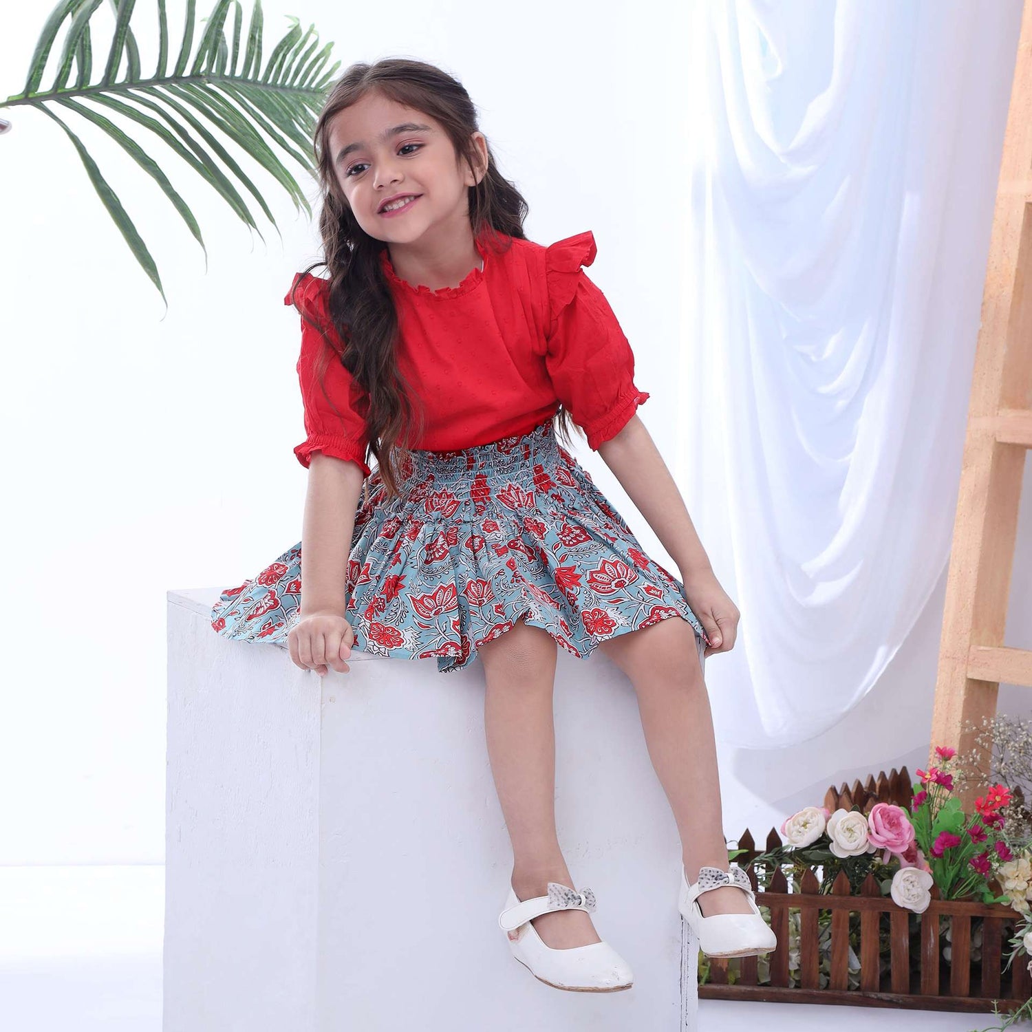 A little girl in teal and coral chinoiserie print skirt with red swissdot blouse with ruffle collar and pleating on bodice