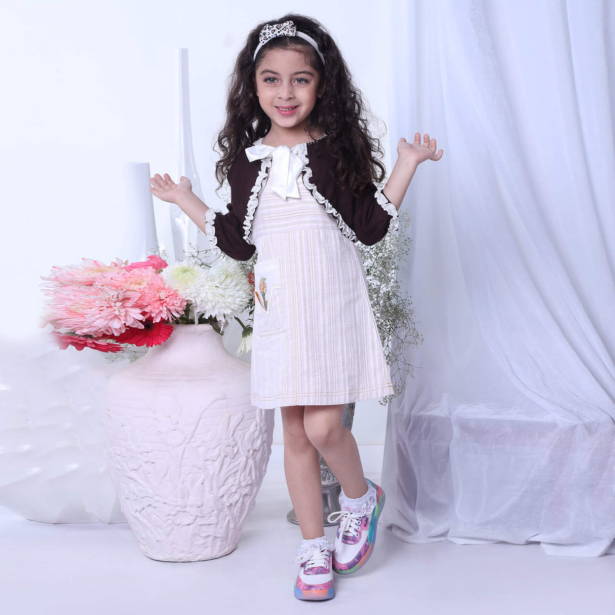 Dancing gracefully, a young girl in an ivory A-line dress paired with a brown bolero embroidered jacket