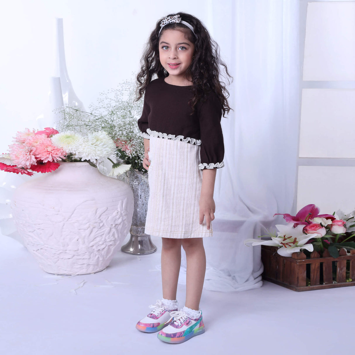 In a side view, a girl showcases an ivory A-line dress paired with a brown bolero embroidered jacket