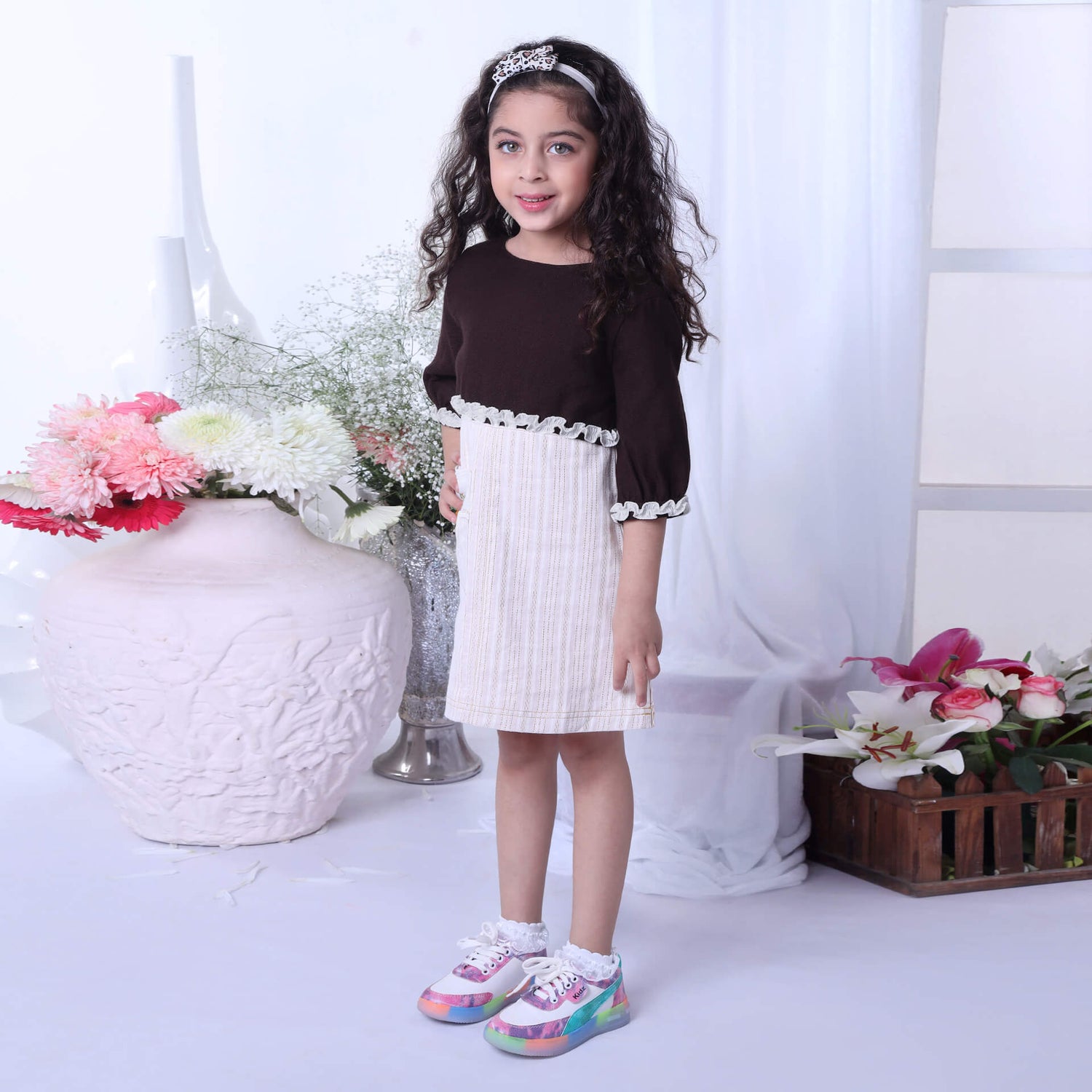In a side view, a girl showcases an ivory A-line dress paired with a brown bolero embroidered jacket