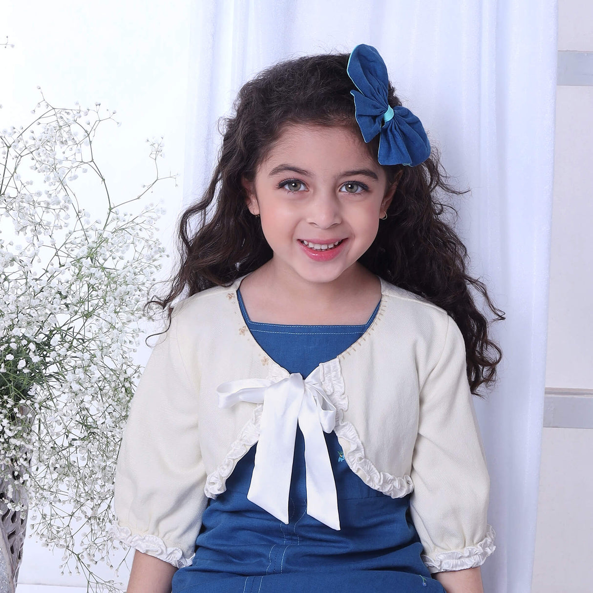 In a detailed shot, a girl wears a blue A-line dress paired with an ivory bolero embroidered jacket