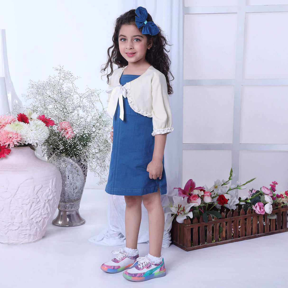 In a side view, a girl showcases a blue A-line dress paired with a brown bolero embroidered jacket