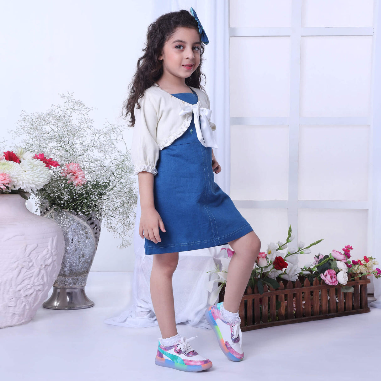 In a blue A-line dress paired with an ivory bolero embroidered jacket, the girl smiles as she strikes a pose