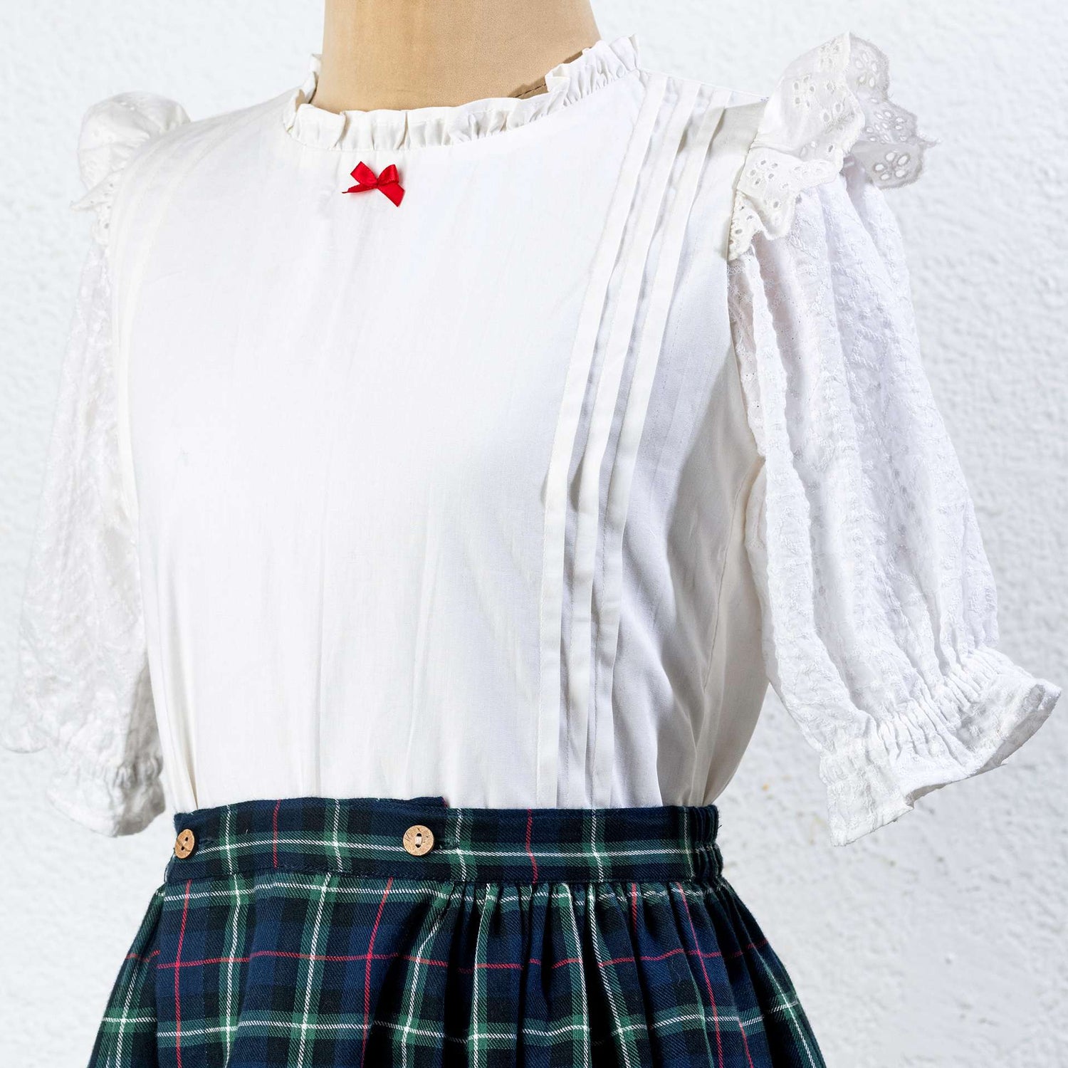 Close-up of tartan wrap skirt in navy blue with wood buttons paired with white bouse with pintucks