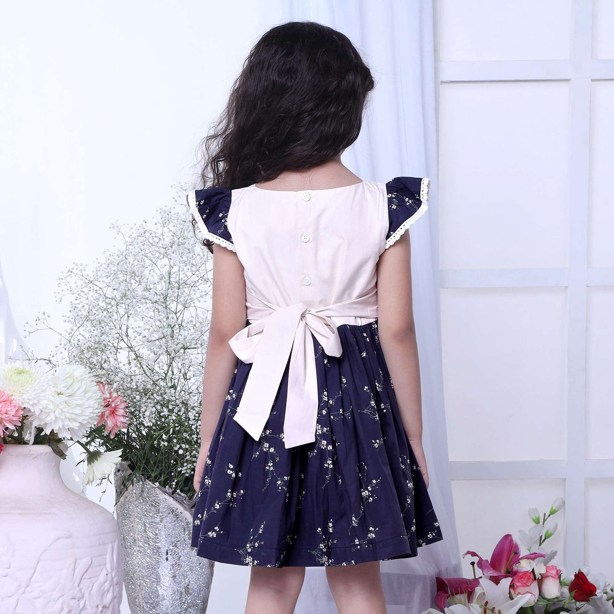 A girl in floral printed cotton navy dress with flutter sleeves, lace trims and hand embroidered bouquet in the yoke