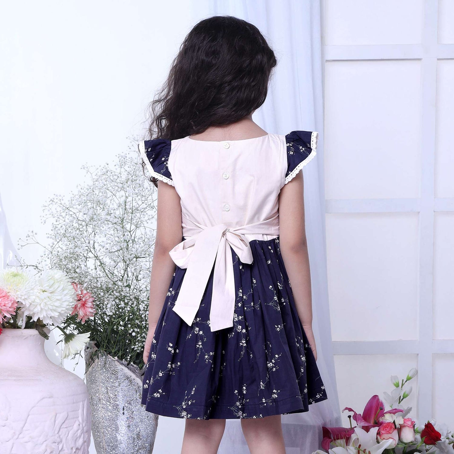A girl in floral printed cotton navy dress with flutter sleeves, lace trims and hand embroidered bouquet in the yoke