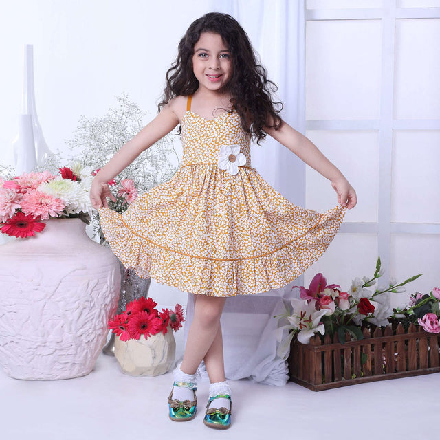 A little girl wearing strappy shoulder dress with floral print in mustard and big flower appliqued on the waist