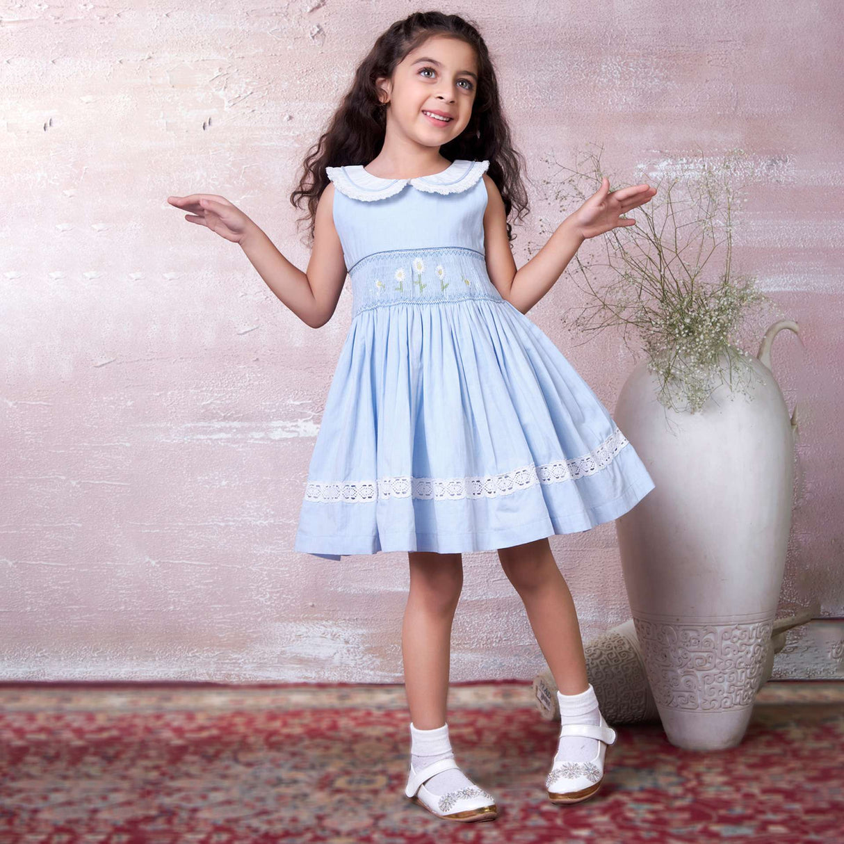 A little girl in blue hand-smocked dress with a lace insert on the skirt and a detailed collar with lace and cord piping