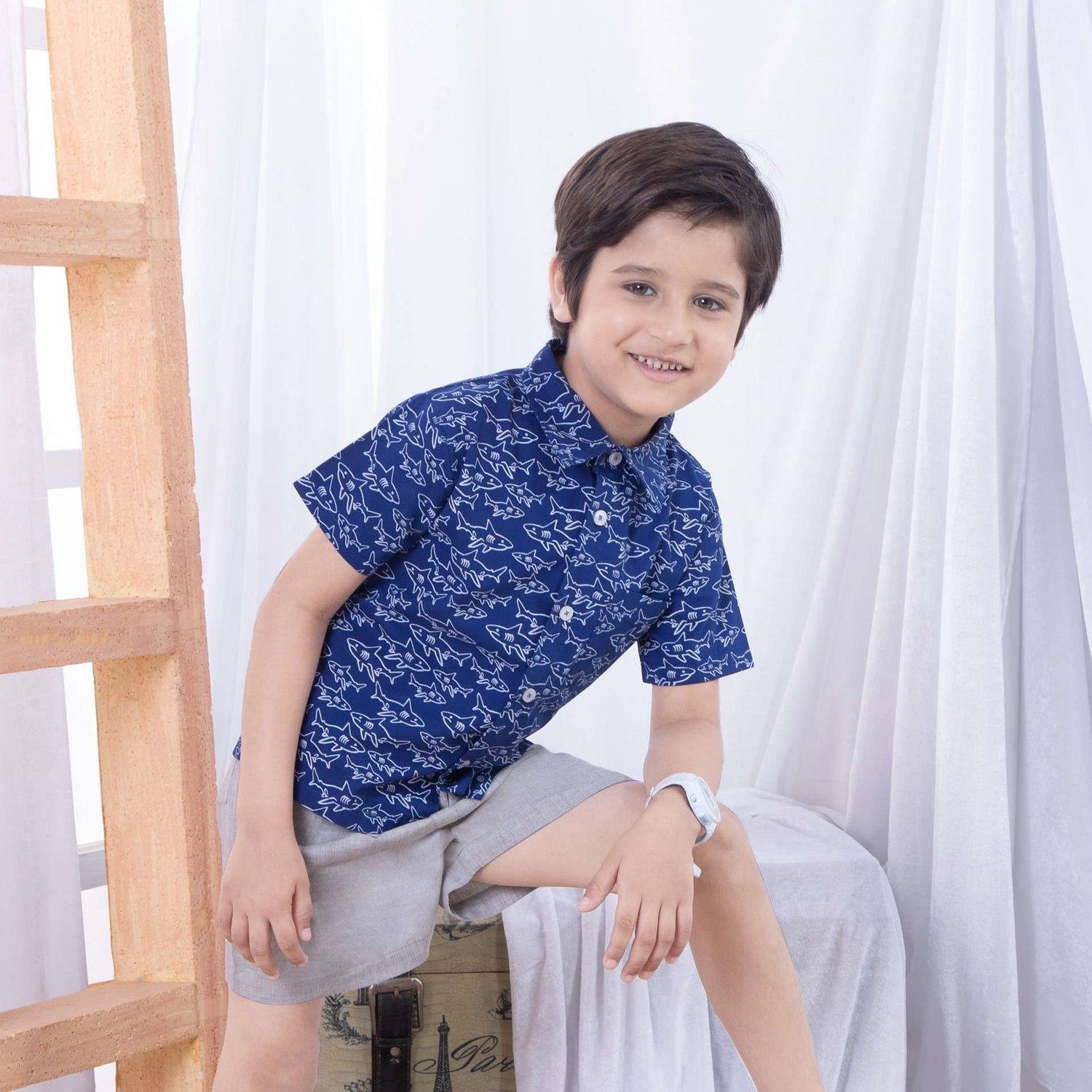 Boy wears a shark print half sleeve shirt and smiles at the camera
