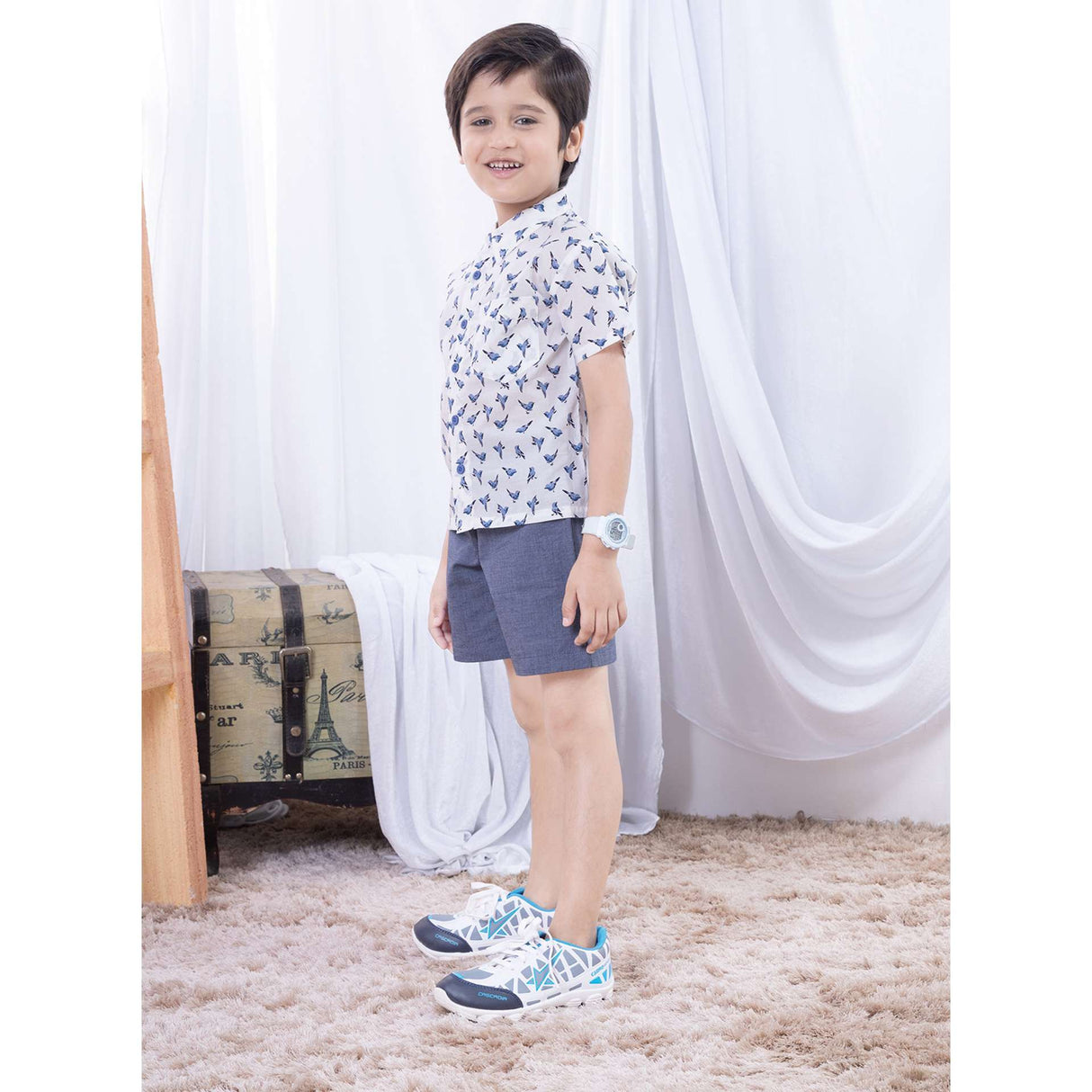 Side view of boy wearing a bird print shirt and navy casual shorts