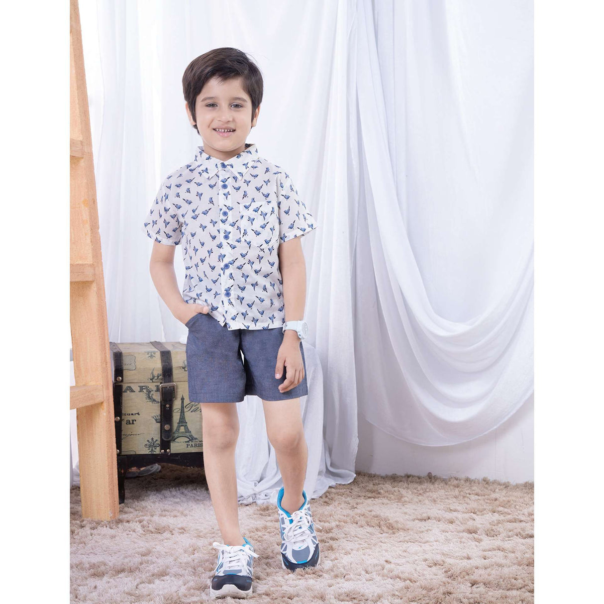 Boys wears a half sleeve shirt in ivory with blue printed birds and blue shorts