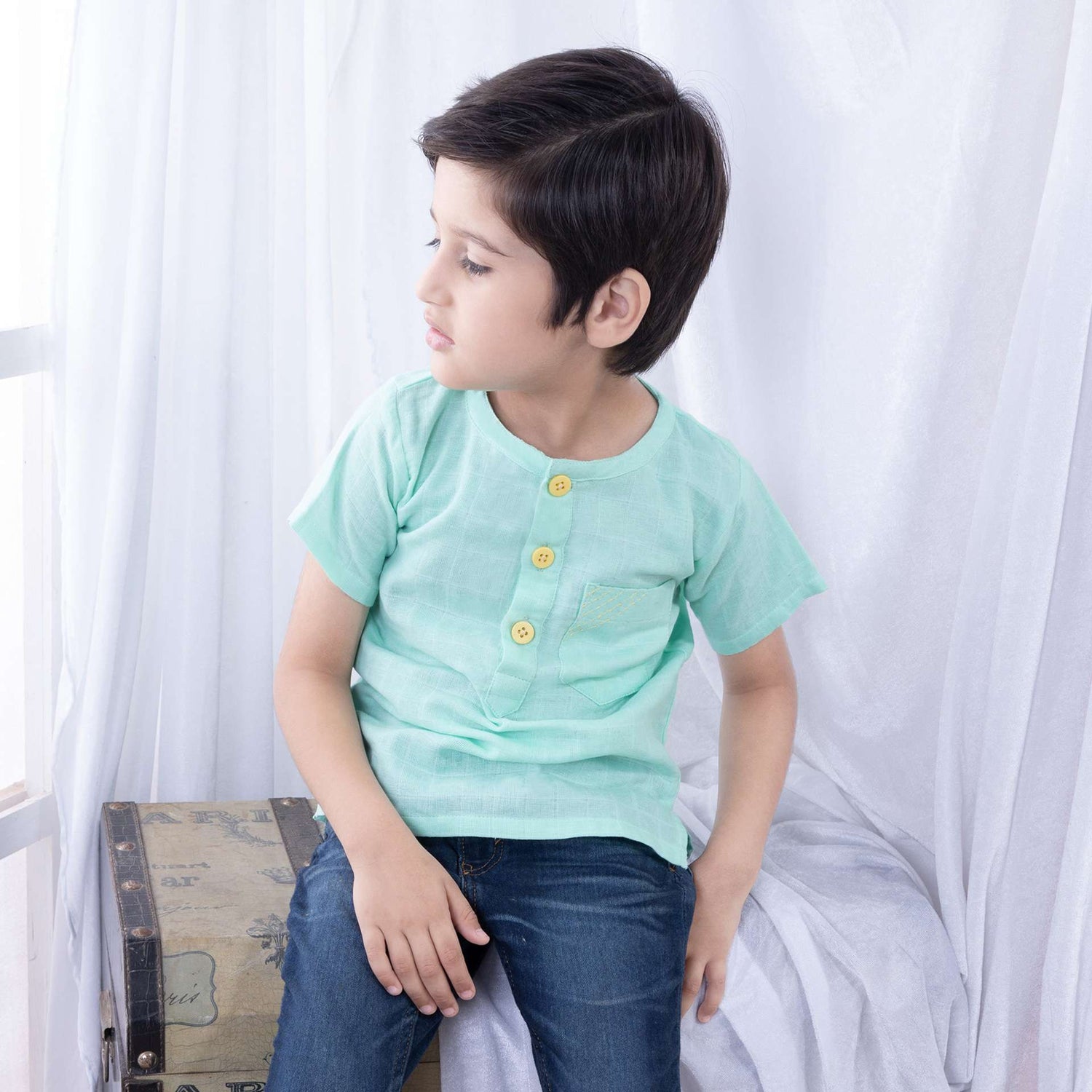 Boy seated wearing jeans and a aqua green polo half sleeve gauze shirt