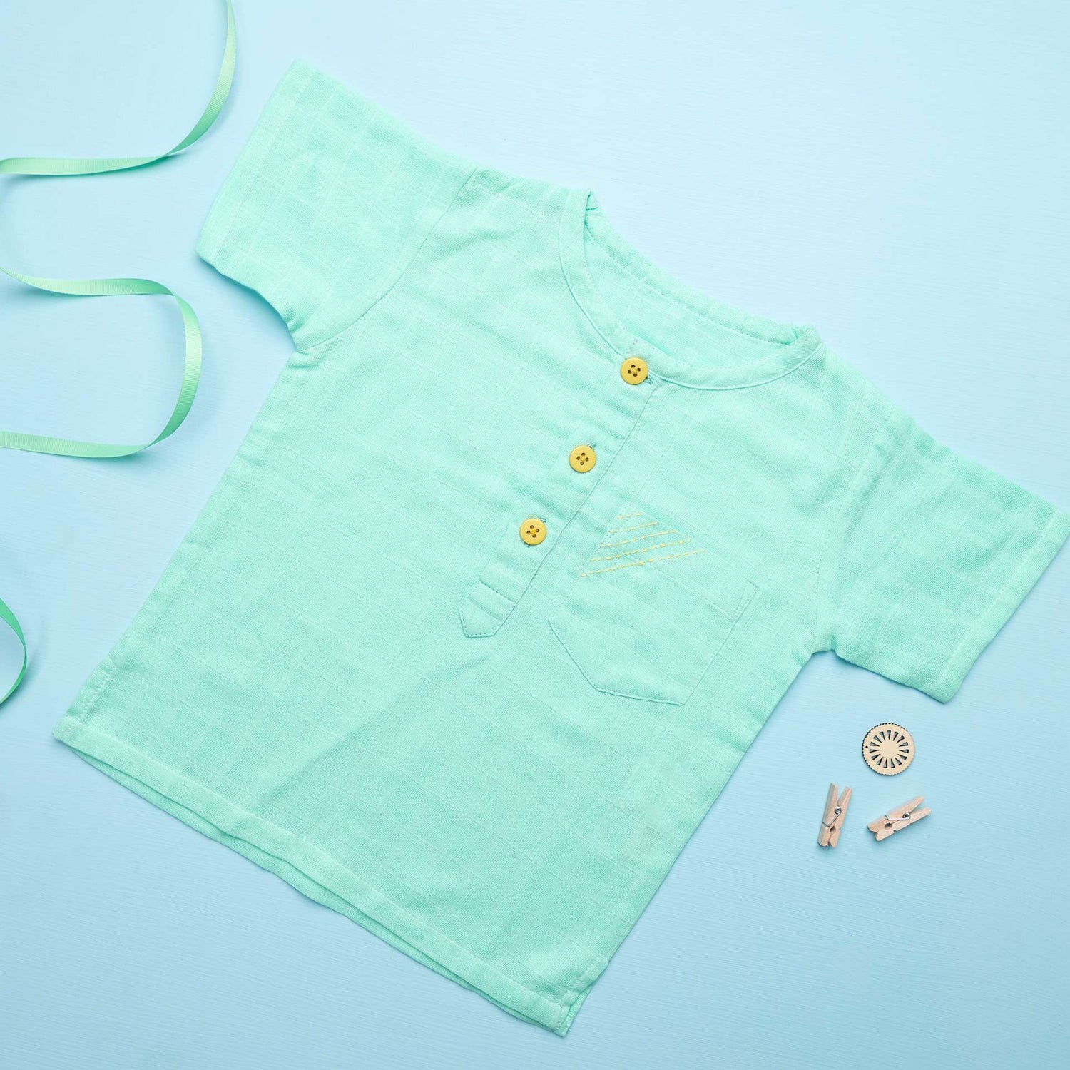 Flatlay of aqua gauze boy's shirt with hand embroidered front pocket and yellow buttons