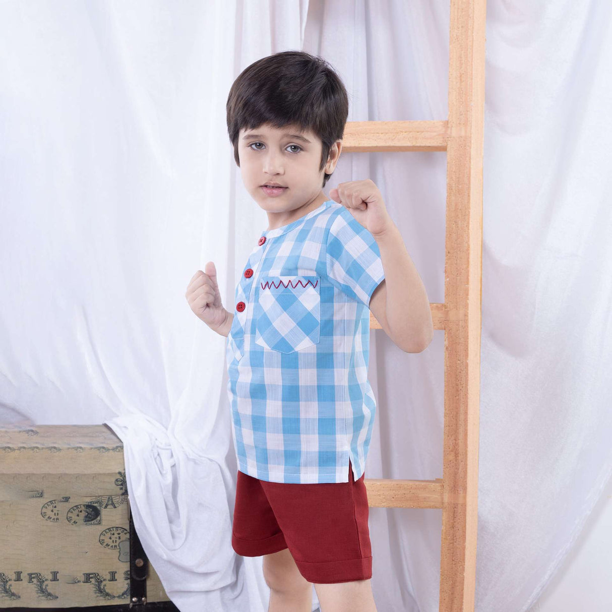 A boy in a striking blue checked shirt with bold red chevron hand-embroidered front pocket and bright red buttons
