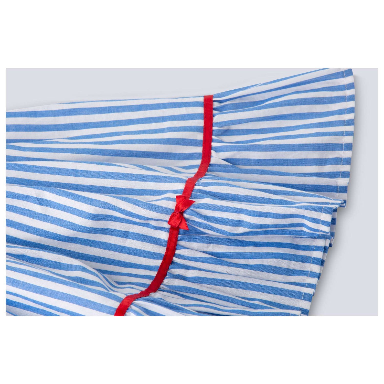 Close-up of hem of blue stripe cotton dress with satin bows on the hem ruffle and bodice, a satin belt at the waist