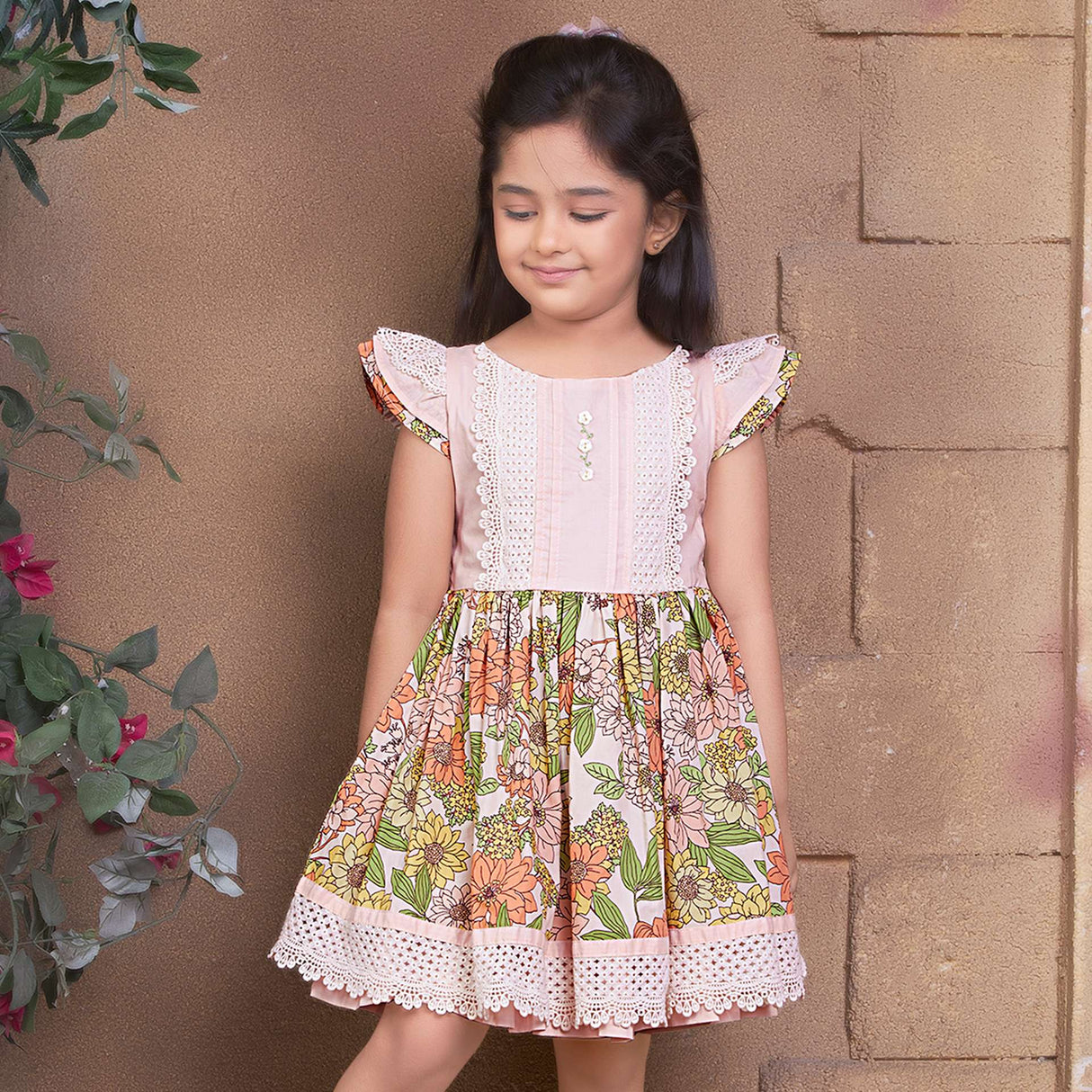 A little girl wearing floral cotton dress with a peach yoke and hem with beautiful lace trims and hand embroidery