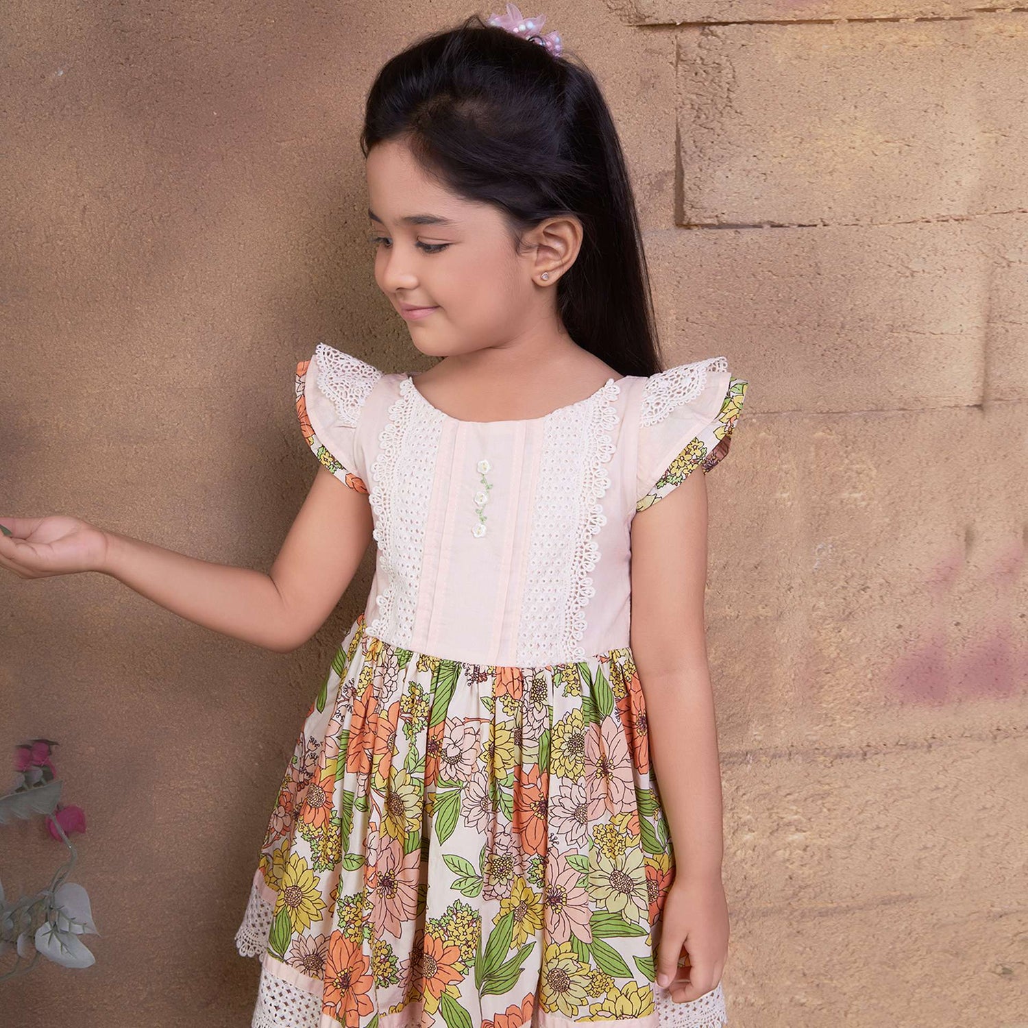 A little girl wearing floral cotton dress with a peach yoke and hem with beautiful lace trims and hand embroidery