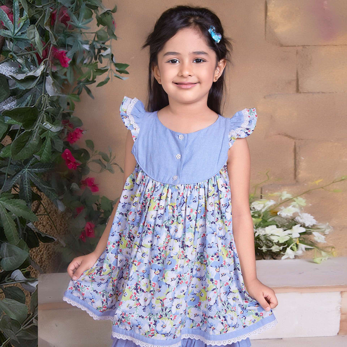 A little girl in blue chambray floral printed cotton dress with flutter sleeves, eyelet lace trims and ruffled hem
