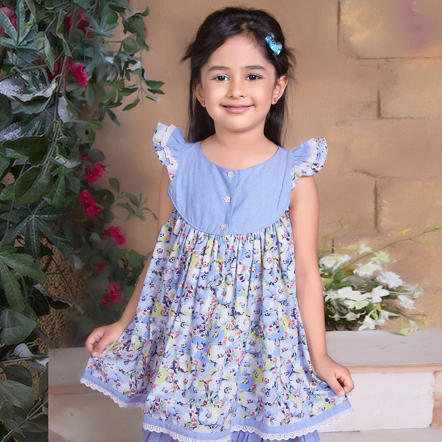 A little girl in blue chambray floral printed cotton dress with flutter sleeves, eyelet lace trims and ruffled hem