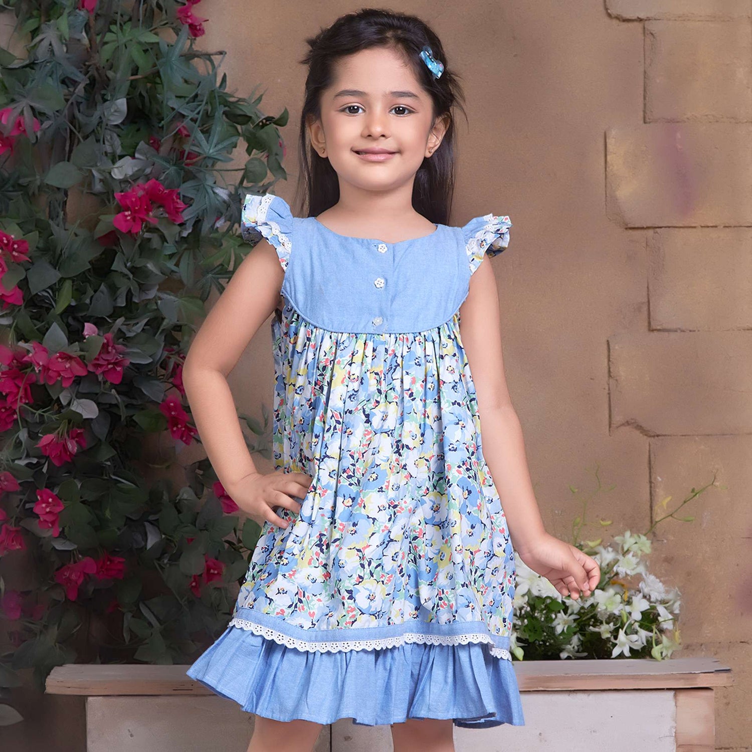 A little girl in blue chambray floral printed cotton dress with flutter sleeves, eyelet lace trims and ruffled hem