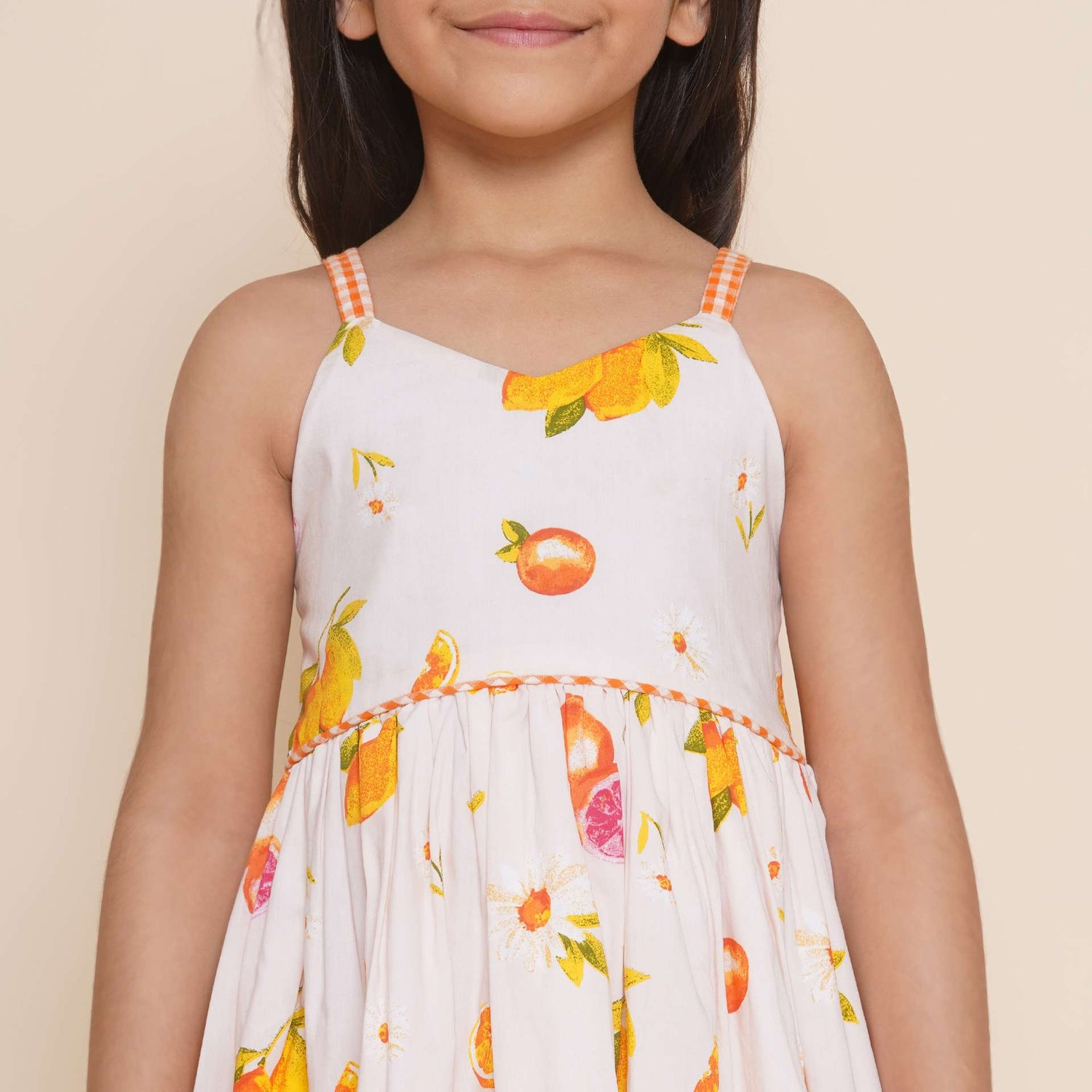 Close-up of pink vibrant fruit print dress with lemons, tangerines and daisies and orange gingham trims